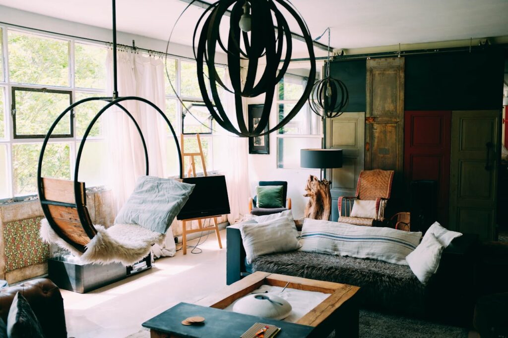 A modern living room featuring plush furniture, hanging chair, and large windows letting in natural light.